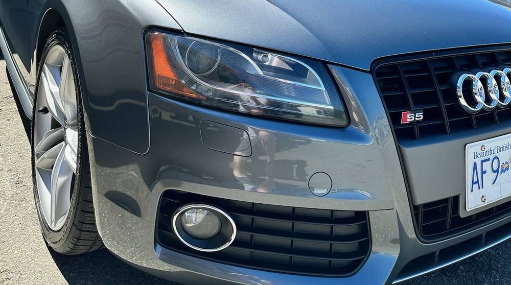 The polished front corner of a grey Audi S5, headlight and wheel