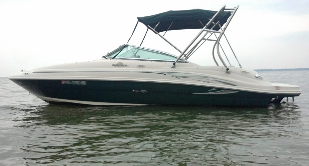 A green-hulled Sea Ray Sundeck with a bimini top, sitting in shallow water
