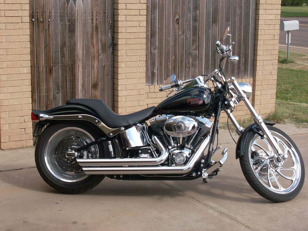A black Harley-Davidson Softail with polished chrome exhaust, engine and wheels, parked on a concrete driveway