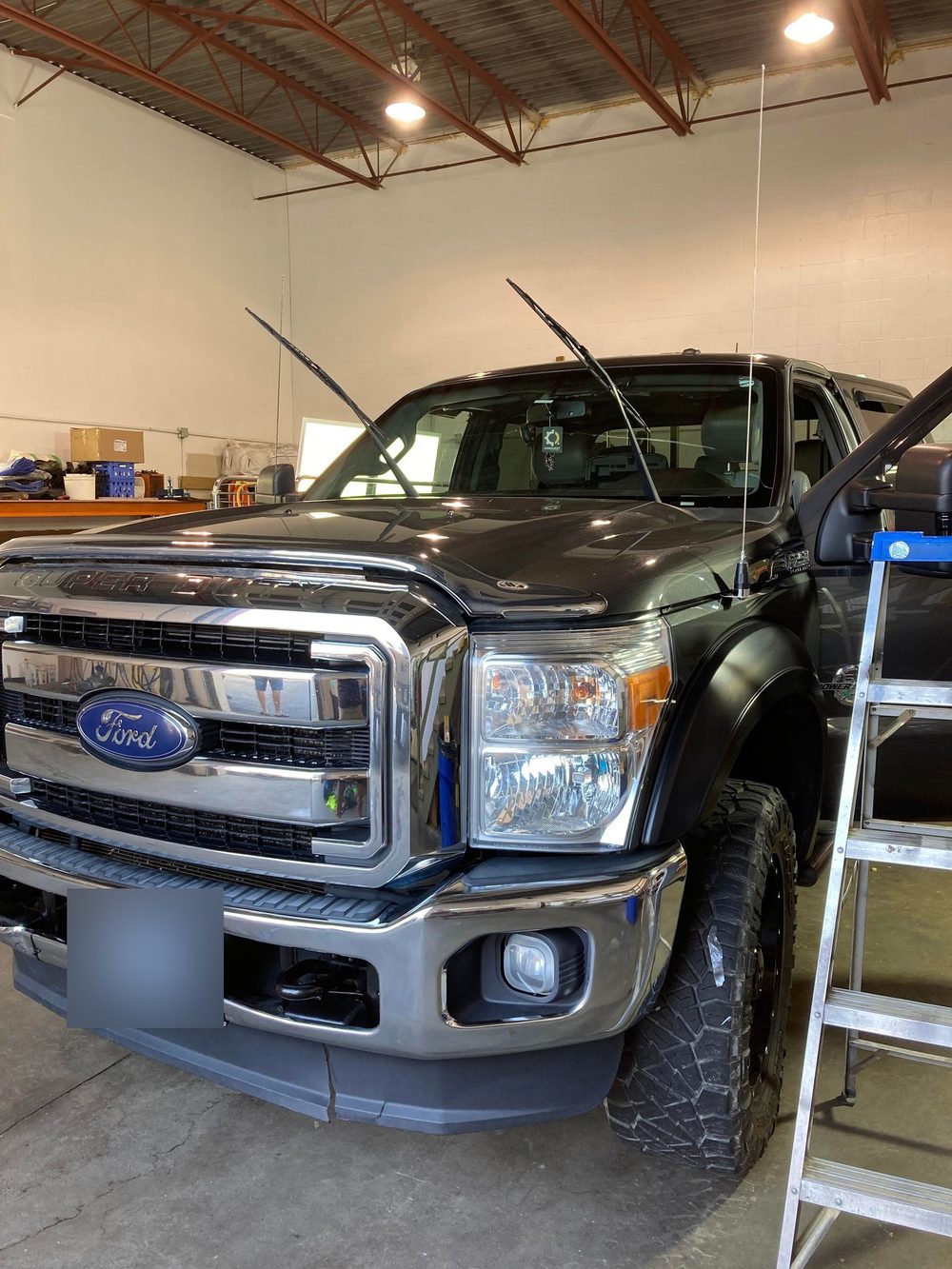 A black Ford F-250 Super Duty parked inside the shop bay, hood and front end in view